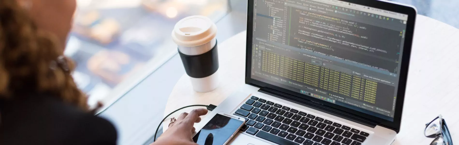 image of a girl sitting on a desk with a laptop, and beside them there is coffee and a mobile phone.