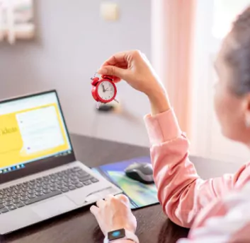 A female taking watch on hand and working on laptop